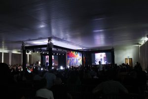 Plateia lotada diante do palco com trelica de iluminacao e teloes de LED